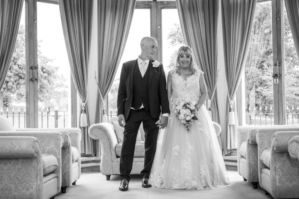 A timeless black and white wedding photograph capturing the groom's emotional gaze as he admires his radiant bride standing in the elegant drawing room of Runcorn Town Hall.