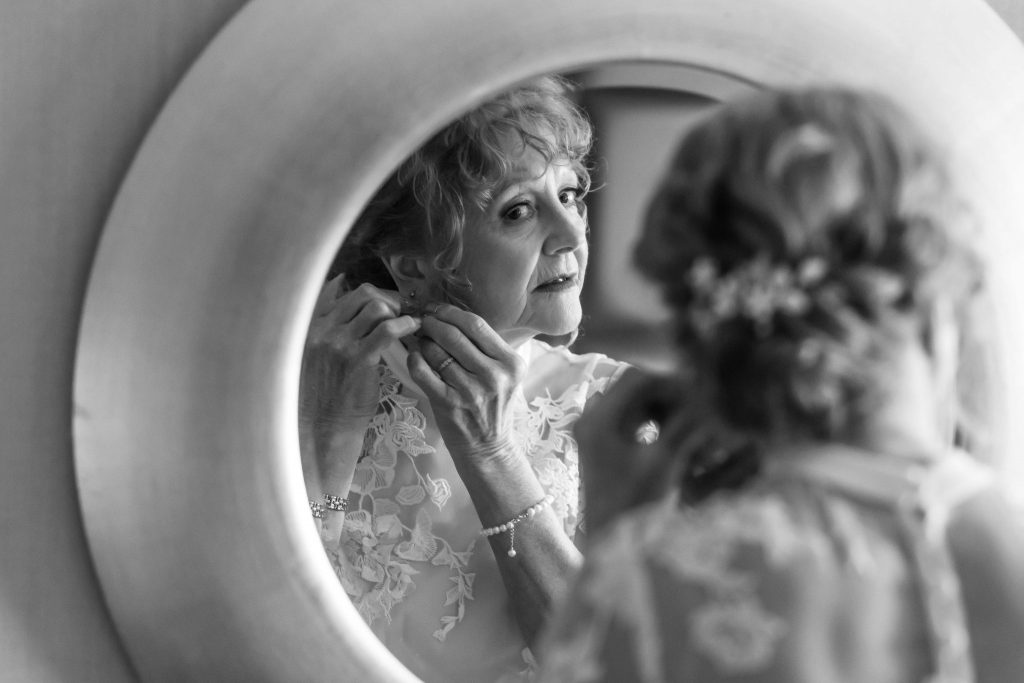 Timeless black & white: Bride adjusts earrings in mirror, anticipation fills the air. #weddingphotography #gettingready