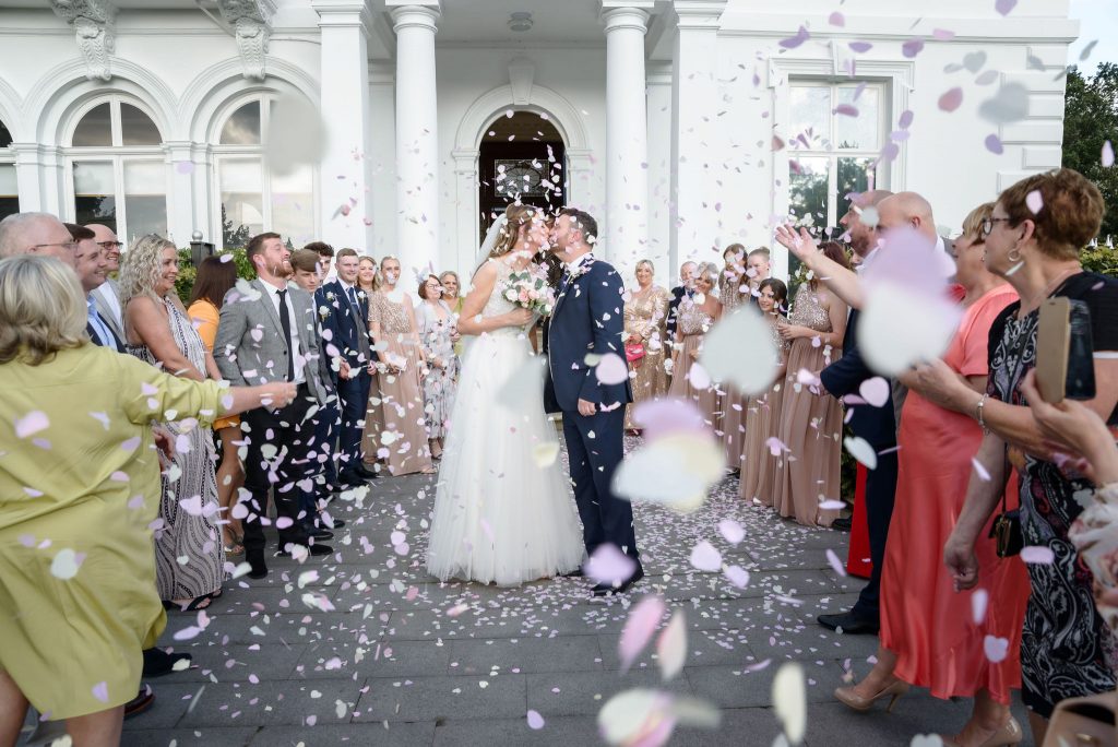 a newly married couple kissing each other with confetti being thrown over them at Runcorn Town Hall during their wedding day