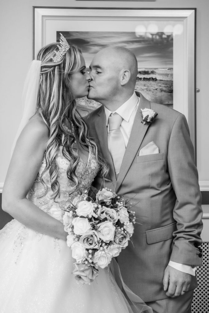 a black and white wedding day portrait photograph of the bride and groom kissing at their wedding in Fleetwood, Lancashire