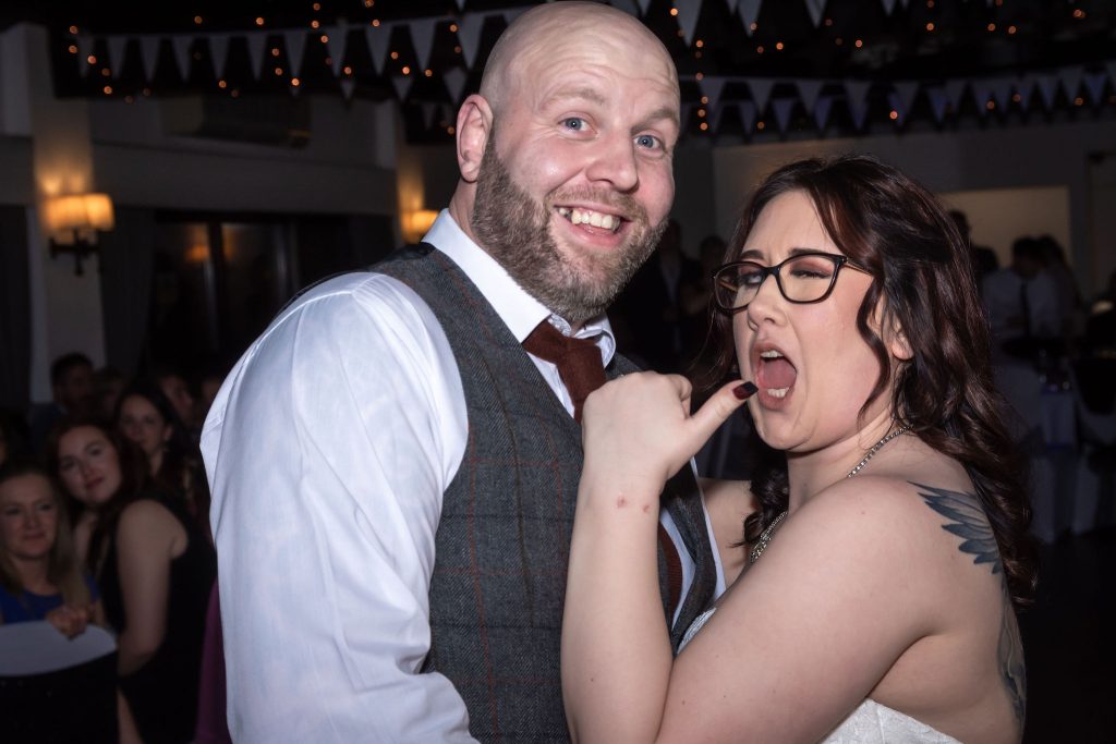 bride winking with her thumb in the air whilst dancing with her groom